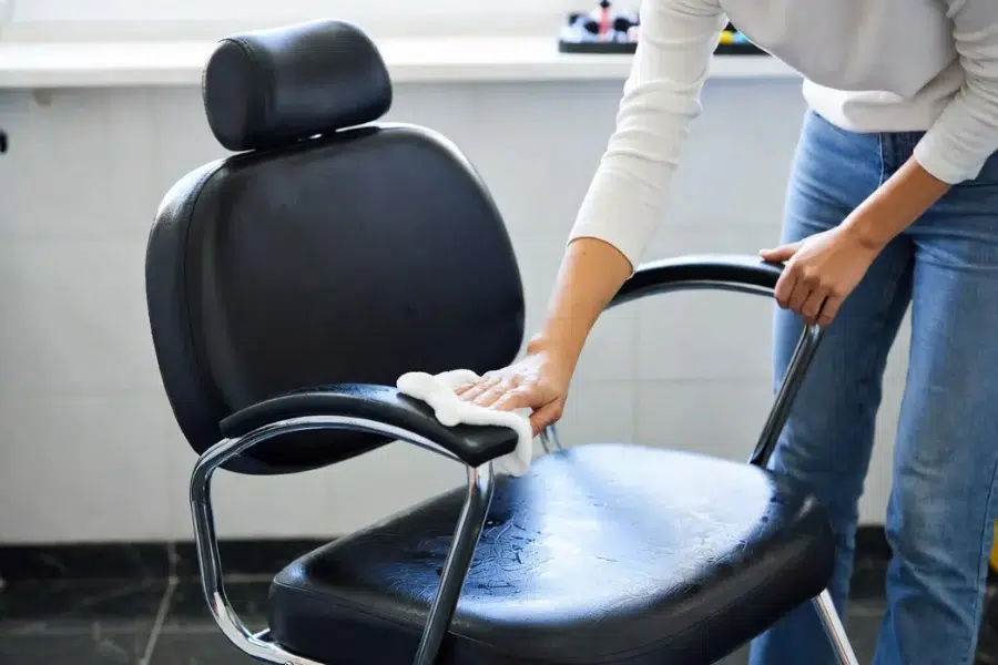 A salon professional cleaning an all-purpose salon chair with a soft microfiber cloth