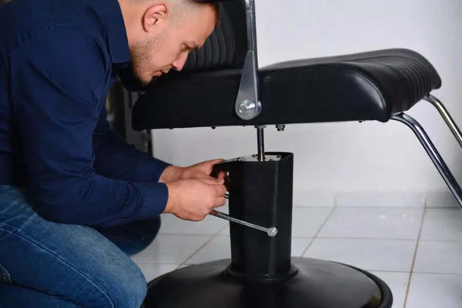 Salon technician inspecting the hydraulic system of an all-purpose salon chair